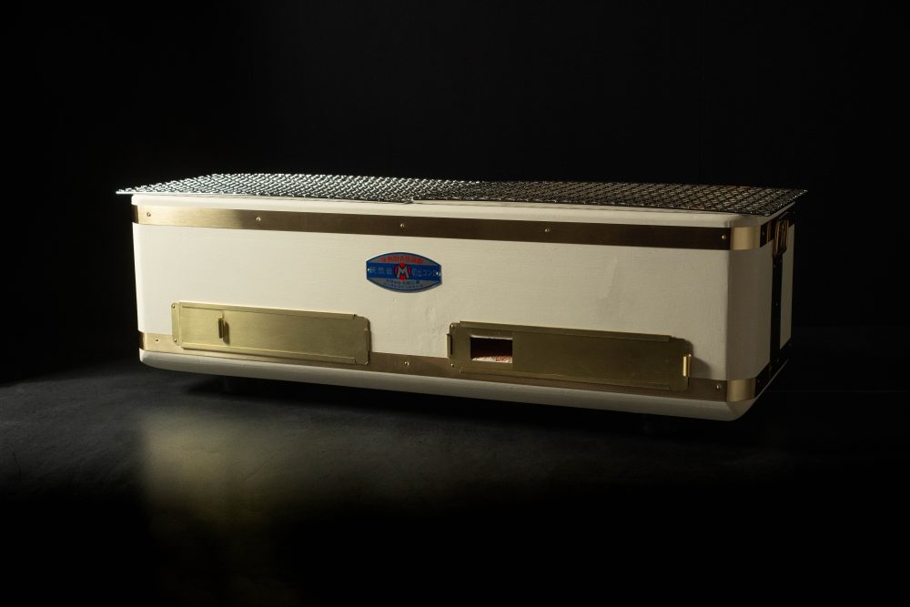 Large rectangular Yakitori Konro charcoal grill with mesh grate, brass accents, and blue Japanese label, displayed on a dark surface.