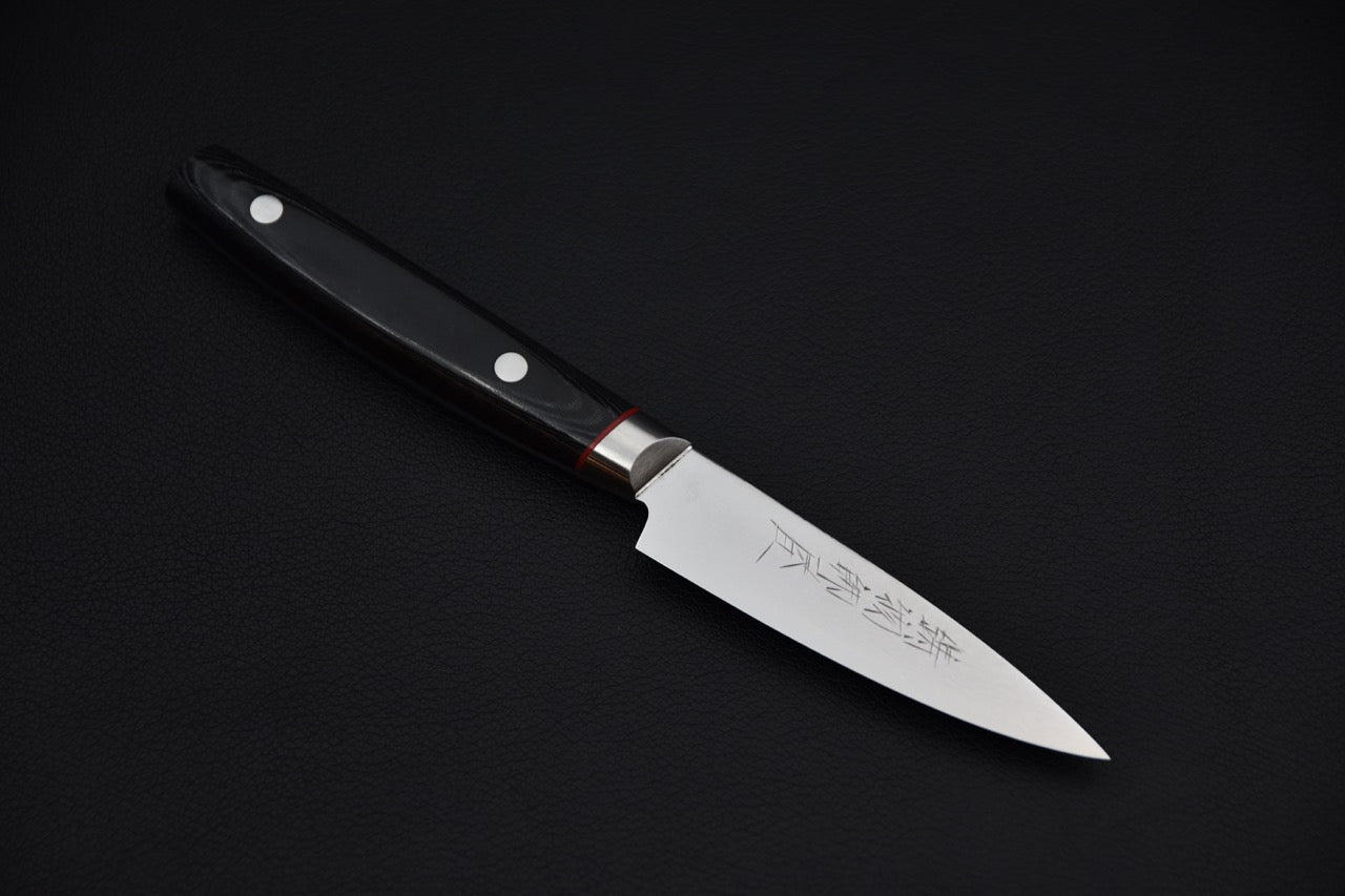 Japanese paring knife with a polished blade and black micarta handle featuring two rivets, displayed on a dark background.