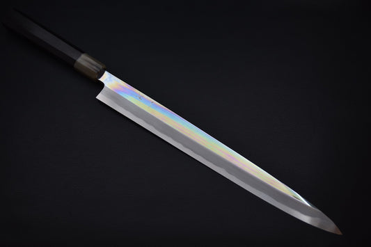 Japanese yanagiba knife with a long polished blade and a dark wa-style wooden handle, displayed on a black background.