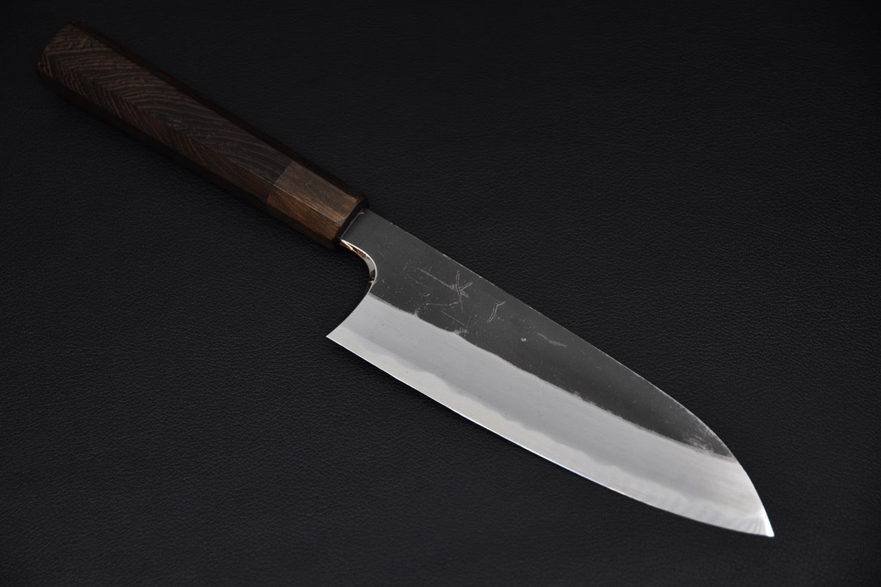 Japanese santoku knife with a polished cutting edge and kurouchi-finished blade, paired with a dark wooden wa-handle, displayed on a black background.