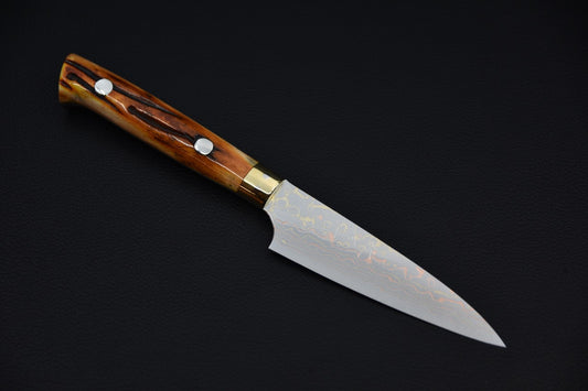 Japanese petty knife with a polished rainbow Damascus blade and a carved horn handle featuring two rivets, displayed on a dark background.