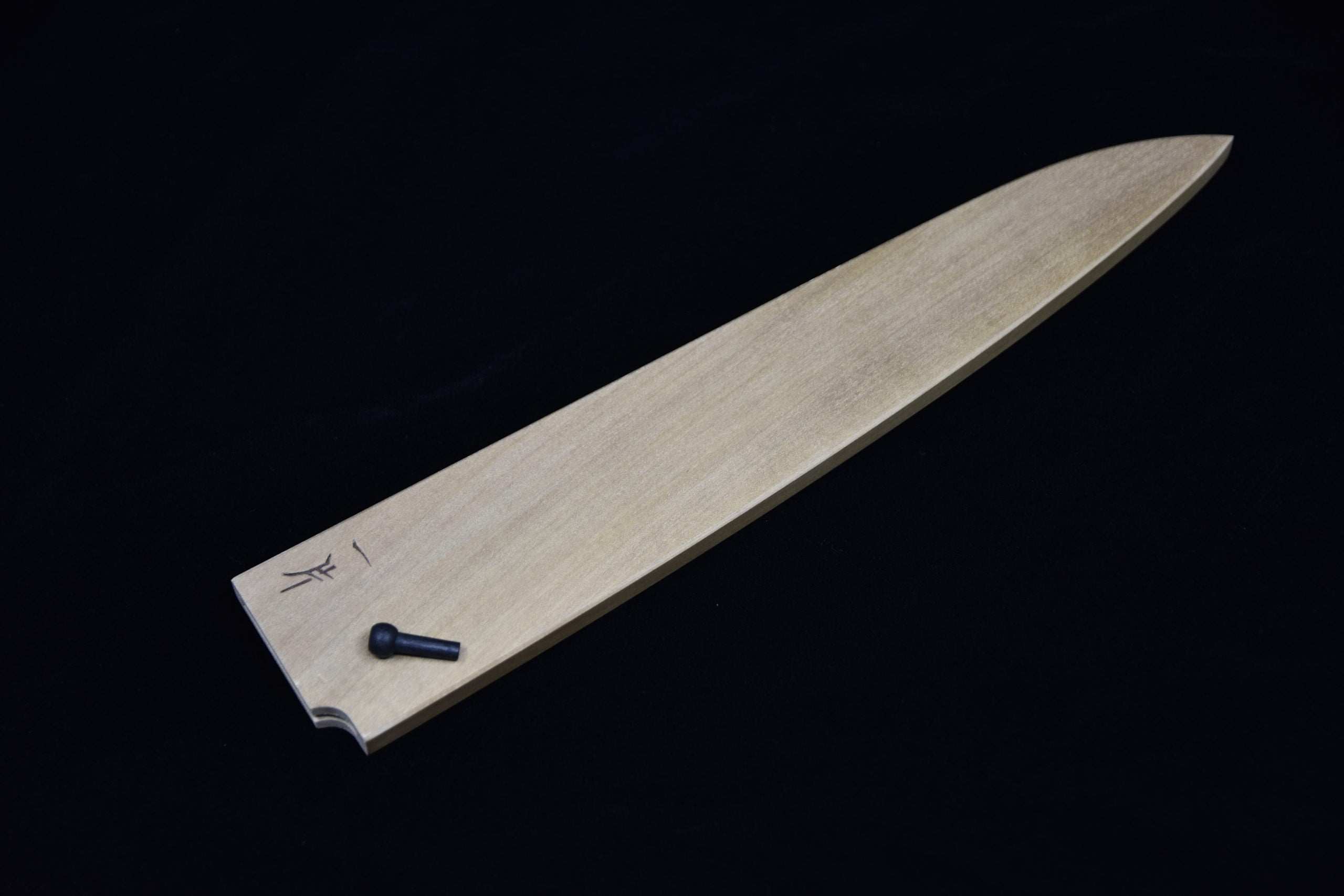 Wooden saya sheath for a Japanese knife, featuring a securing pin and decorative engraving, displayed on a black background.
