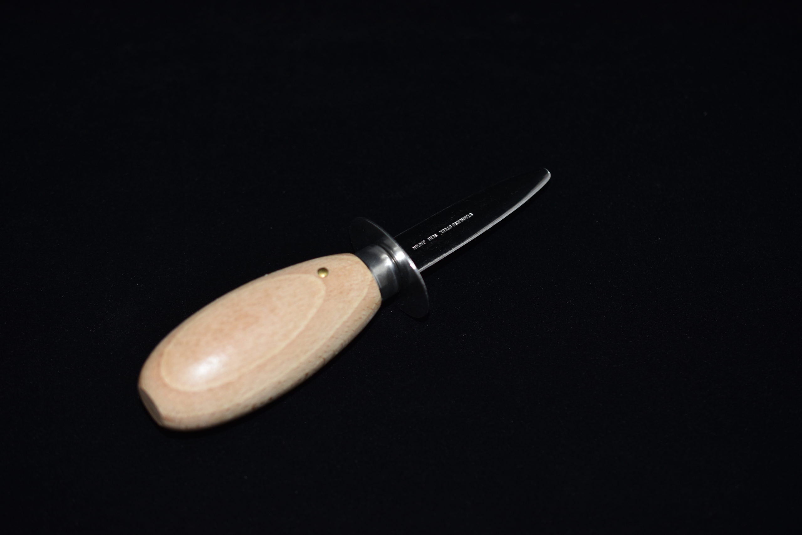 Oyster shucking knife with a curved blade and rounded wooden handle, displayed on a black background.